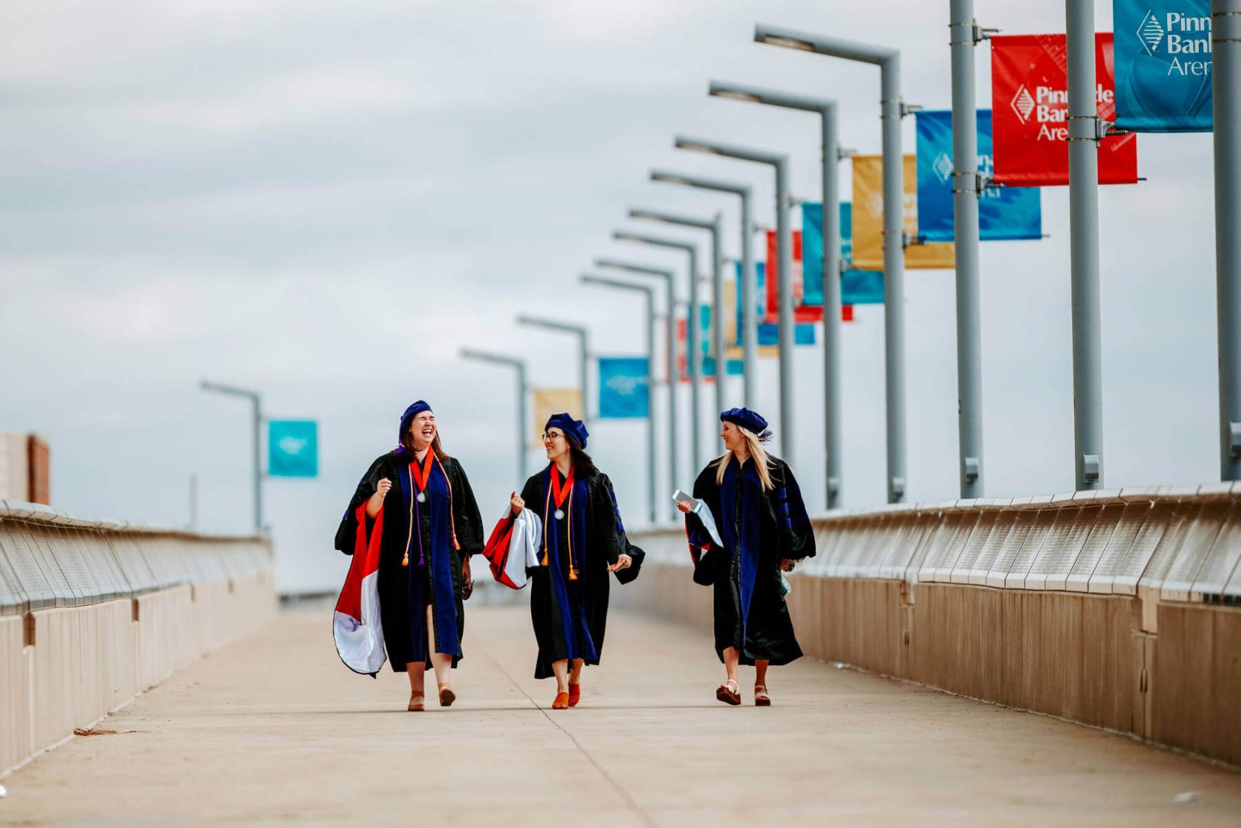 Graduates walk on bridge towards Pinnacle Bank Arena