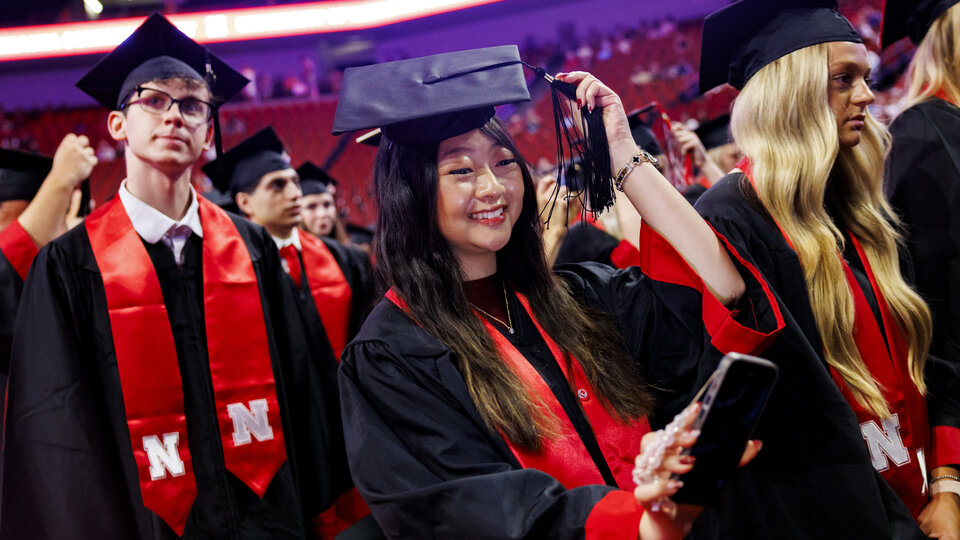 Graduates in caps and gowns celebrating at a commencement ceremony in a large venue.