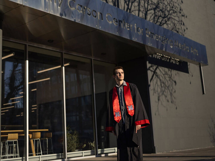 Student in graduation gown and sash standing outside Johnny Carson school