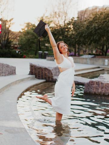Graduate holding up cap while standing in fountain