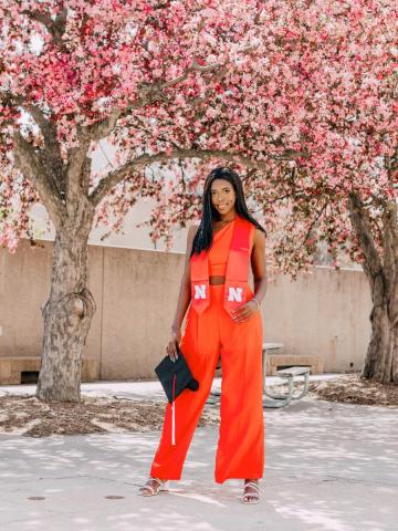 Grad in red outfit standing in front of blooming trees