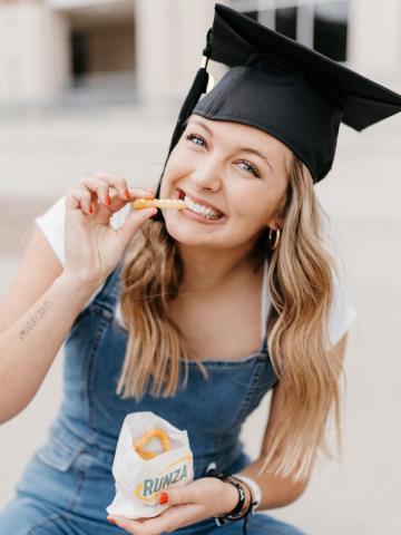 Graduate in overalls eating a french fry