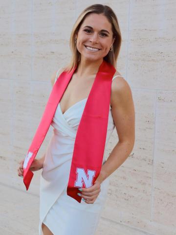 Grad with sash in white dress by stone wall