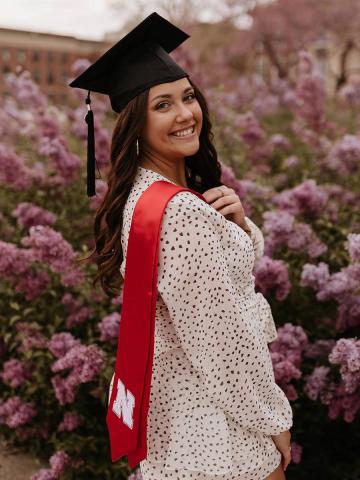 Graduate with cap and sash in front of blooming trees