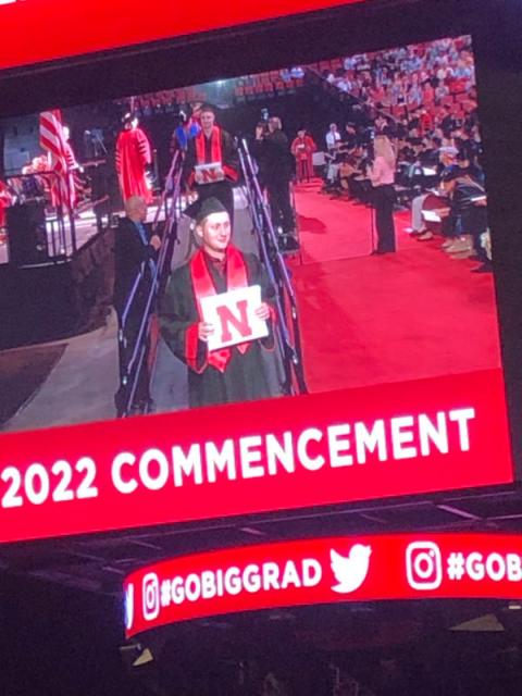 Graduate on big screen at arena posing with diploma