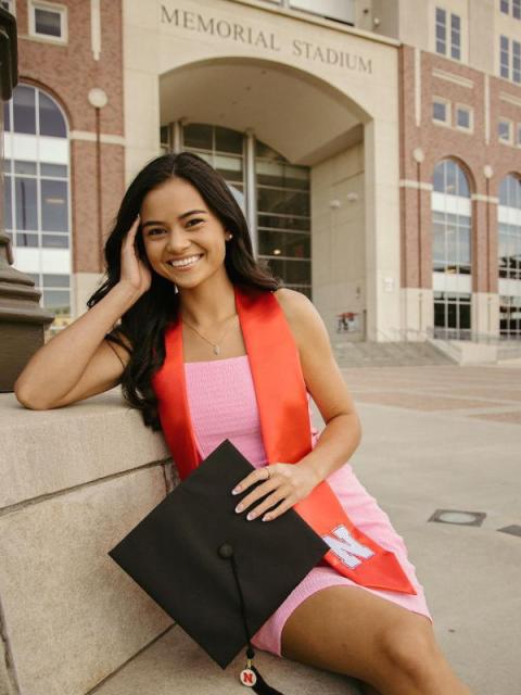Student in pink dress and graduation hat posing in front of Memorial Stadium
