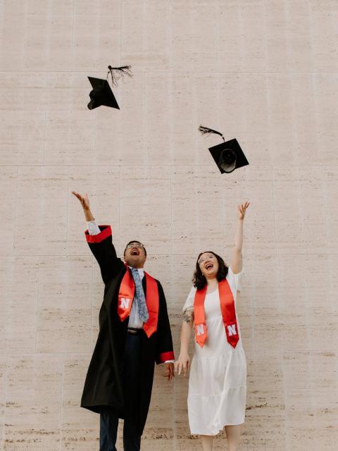 Two students throwing graduation caps in air