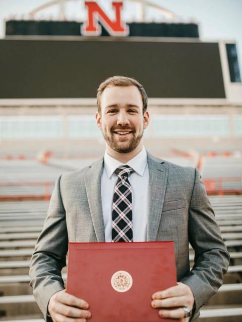 Graduate in suit holding diploma inside Memorial stadium