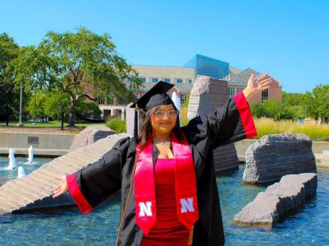 Graduate in cap and gown posing in front of water fountain